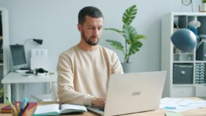 Man working on a laptop at a desk under pressure.