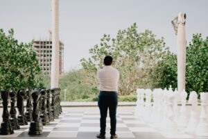decision making of man standing between giant chess pieces on a board