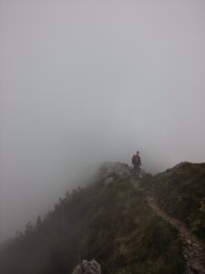 man walking under uncertainty of weather conditions on hill with fogs